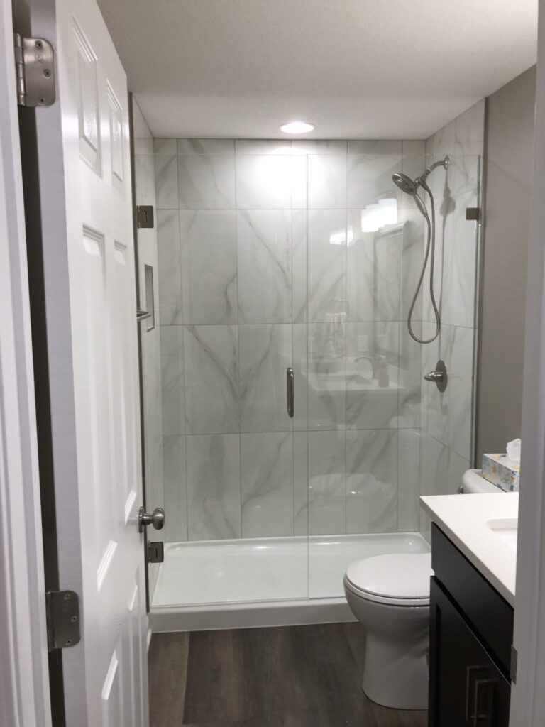 Modern bathroom featuring a glass-enclosed shower, toilet, and white countertop with dark cabinetry on a wooden floor.