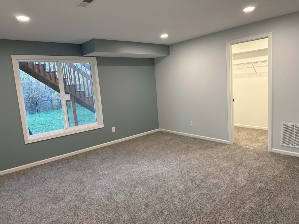 A carpeted room with recessed lighting, a large window, and a doorway leading to a closet.