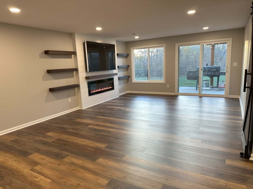 Spacious empty room with wood flooring, wall-mounted fireplace, shelves, and large sliding glass door leading outside.