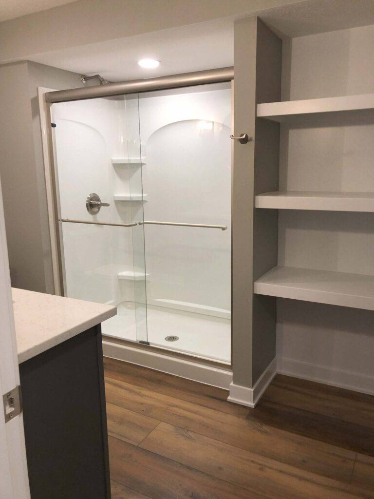 Bathroom with glass-enclosed shower, built-in shelves, and wood flooring.