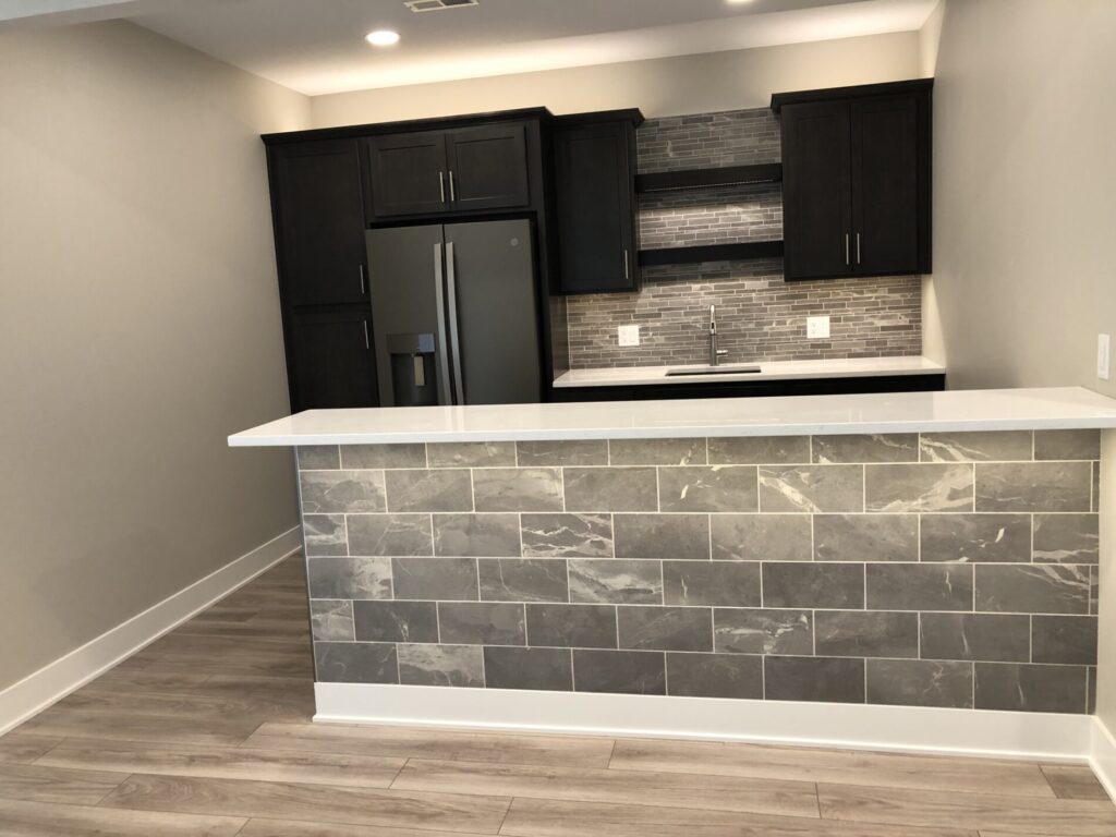 Modern kitchen with dark cabinets, stone backsplash, gray tiled island, and stainless steel refrigerator.