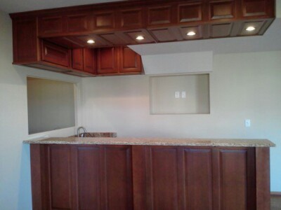 A kitchen with dark wooden cabinets, granite countertop, built-in lighting, and a small sink on the left side.