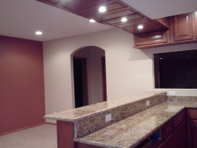 Modern kitchen with granite countertops, wooden cabinets, and recessed lighting, adjacent to an open room with a red accent wall.