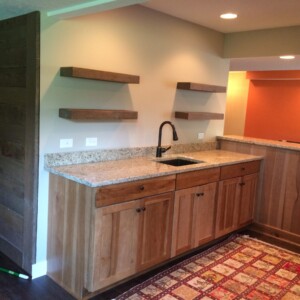 Kitchen area with wooden cabinets, granite countertop, sink, and floating shelves on the wall. Rectangular rug on the floor.