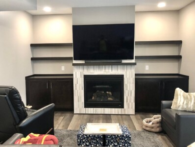 Living room with a wall-mounted TV above a fireplace, flanked by dark wood cabinets and shelves, and furnished with seating.