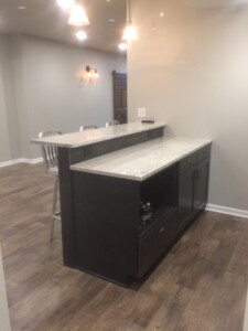 Modern kitchen with a two-tier island, marble countertops, wooden cabinets, and metal barstools on wooden flooring.