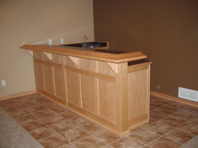 A wooden home bar with a countertop and built-in sink, set on a tiled floor with a beige and brown wall background.