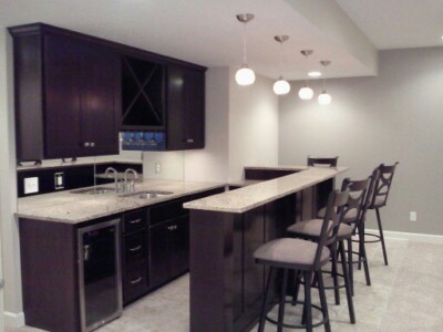 Modern kitchen with dark cabinets, a dual-level countertop, bar stools, and hanging pendant lights.