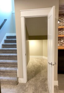 Open door leading to a small carpeted room with slanted ceiling, adjacent to carpeted stairs and a brick wall.