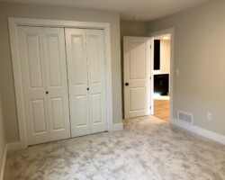 A carpeted room with closed double closet doors and an open door leading to a hallway.