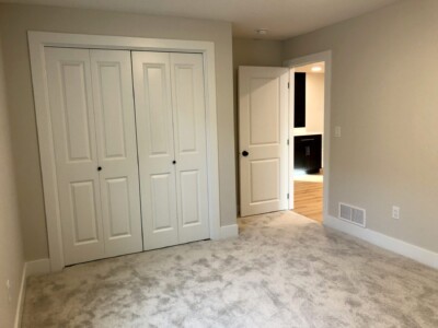 A carpeted room with closed double closet doors and an open door leading to a hallway.