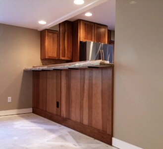 Wooden kitchen counter with built-in cabinets and a stainless steel refrigerator under recessed lighting.