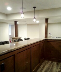 A basement bar area with wooden panels, a countertop, pendant lights, and leather chairs.