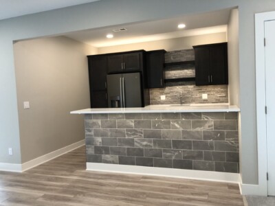 Modern kitchen with dark cabinets, stainless steel fridge, gray tile backsplash, and a tiled island with white countertop.