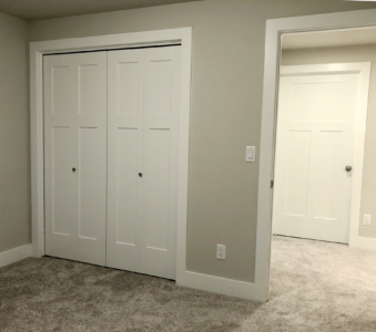 A beige room with carpet, featuring a double door closet and an open doorway leading to another room with a closed door.