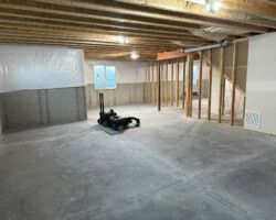 Unfinished basement with exposed beams, plastic-covered walls, and a toolbox in the center on a concrete floor.