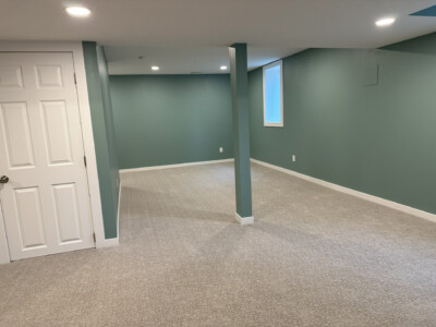 Empty room with green walls, beige carpet, and white door under ceiling lights.