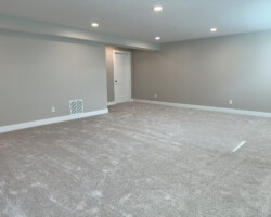 Empty, carpeted room with gray walls, white trim, recessed ceiling lights, and a closed white door on the left wall.