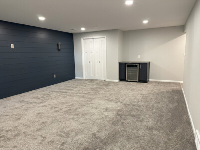 Carpeted room with gray walls, dark accent wall, recessed lighting, a small bar with a mini fridge, and double doors.