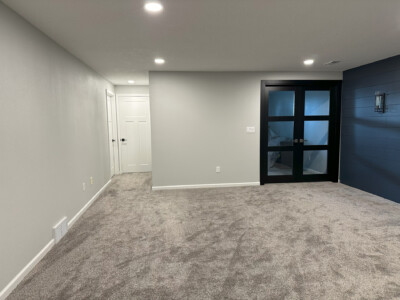 A carpeted room with gray walls, recessed lighting, a black framed glass door, and white double doors on the left.
