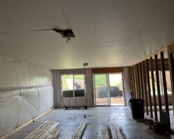 Room under renovation with unfinished drywall, exposed wooden studs, and construction materials on the floor.