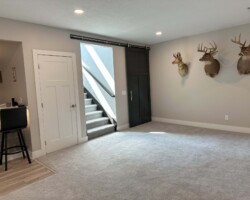 Room with carpet flooring, a sliding door, and stairs. Mounted deer heads on the wall. Bar area partially visible.