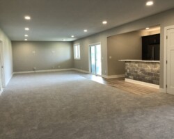 Spacious empty room with carpet, recessed lighting, sliding glass doors, a partial kitchen visible with a tile bar area.