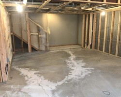 Unfinished basement with exposed wooden framing, concrete floor with visible cracks, and overhead light bulbs.