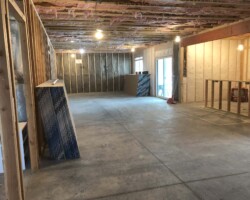 Partially finished basement with exposed framing, insulation, and concrete floor; construction materials are stacked on the left.