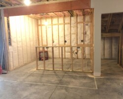 Partially constructed room with exposed wooden framing and insulation on walls, unfinished ceiling and concrete floor.